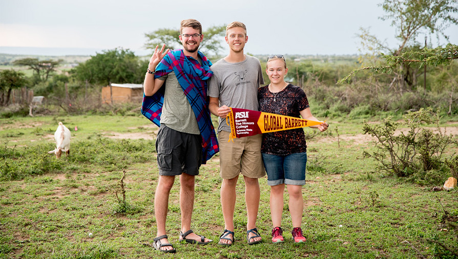 Three Barrett students in a field with a Global Barrett pennant