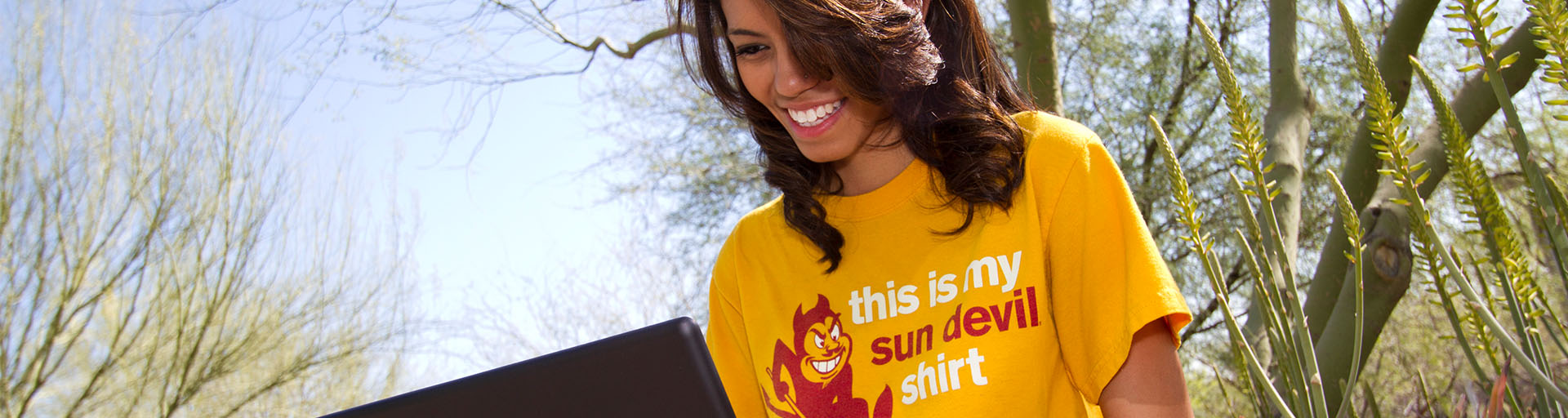 ASU student wearing gold t-shirt, working on a laptop